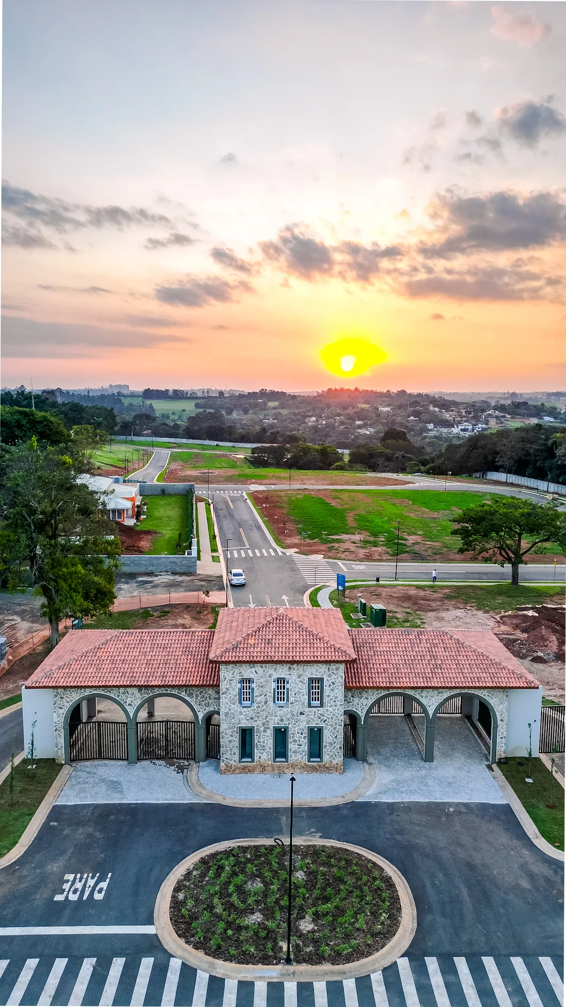 Vista aérea da portaria e das ruas do Reserva Village Prado, com o sol se pondo no horizonte