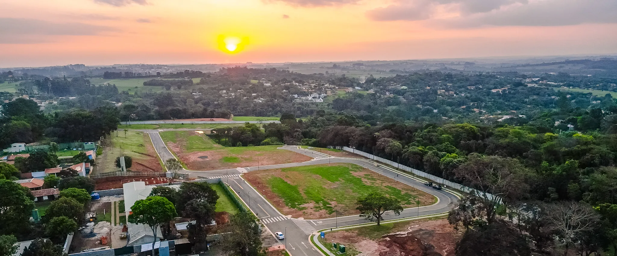 Vista aérea do Reserva Village Prado ao pôr do sol, com as ruas internas, a mata e o horizonte